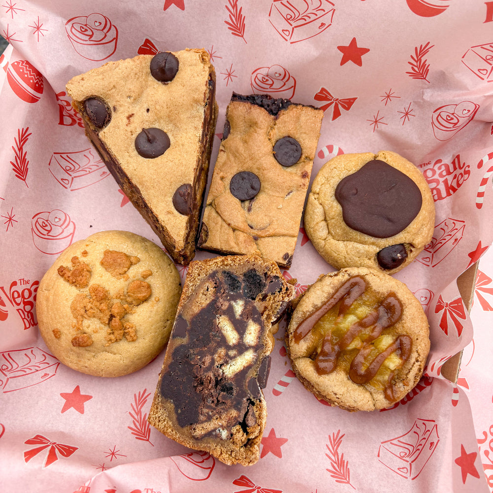 Assorted cookies on a pink paper with 'The Vegan Bakes' branding.