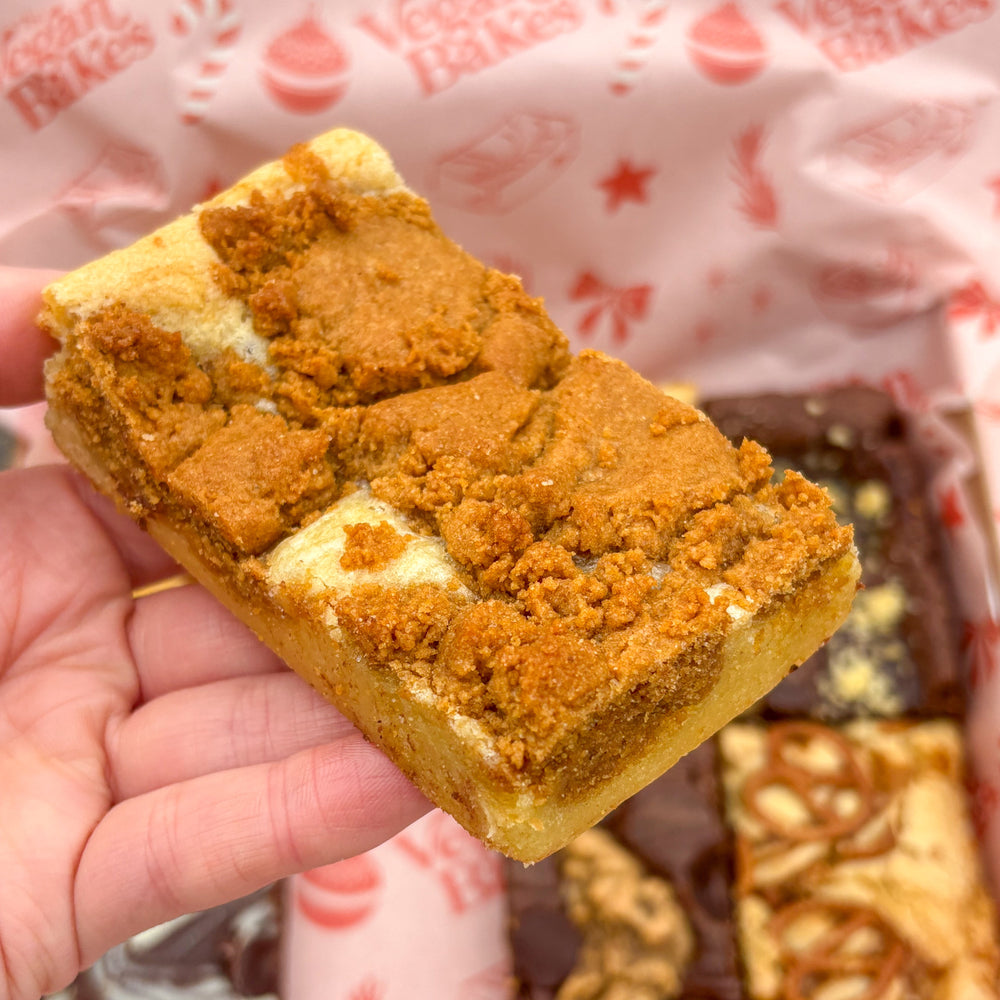 Hand holding a square piece of cake with a crumbly topping against a patterned background