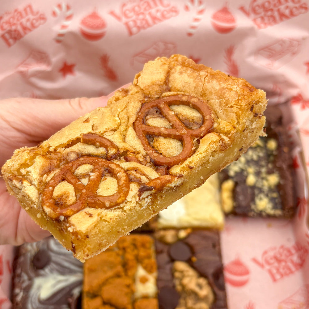 Hand holding a blondie with pretzels and salted caramel filling, with a patterned background.