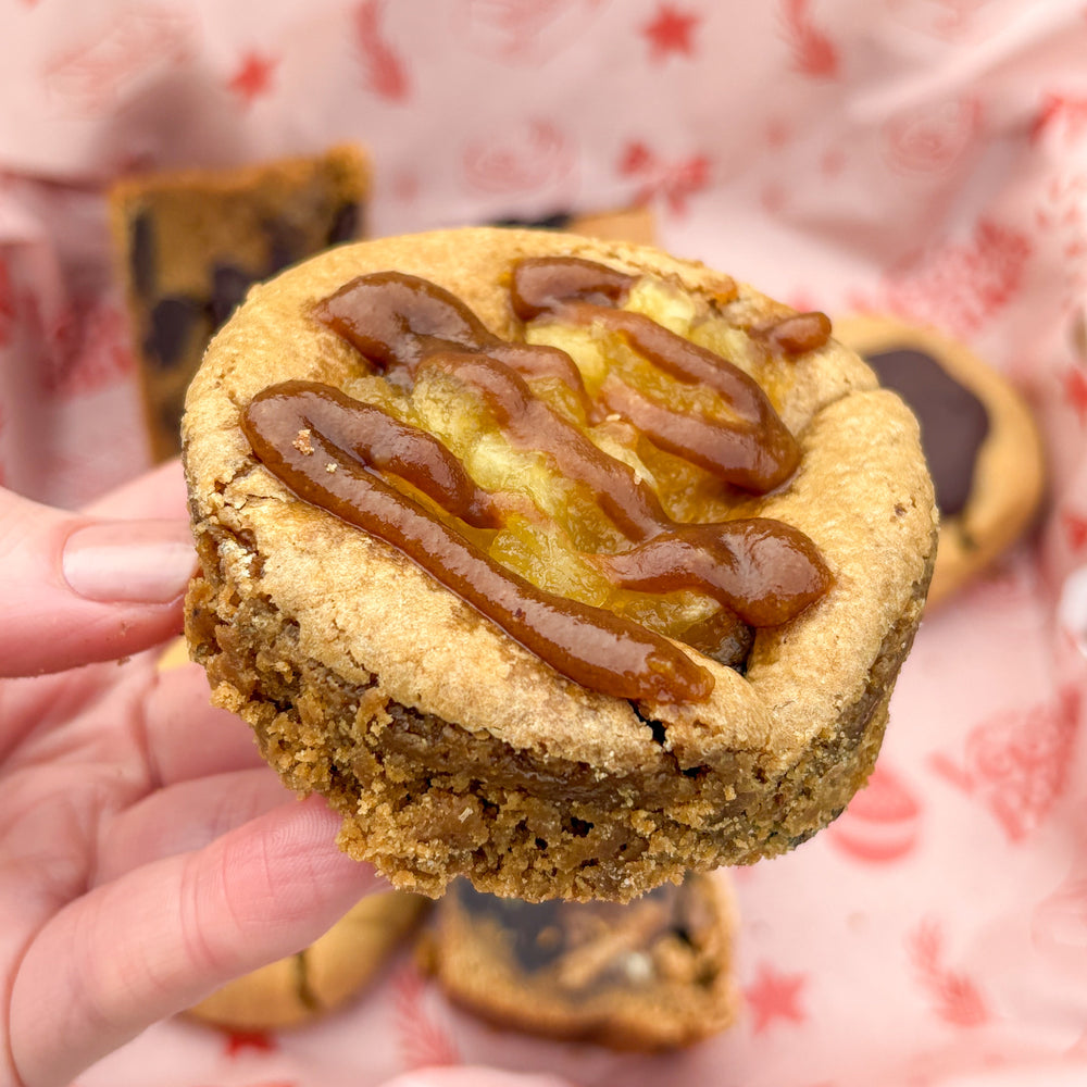 Cookie with caramel drizzle held by a hand against a patterned background