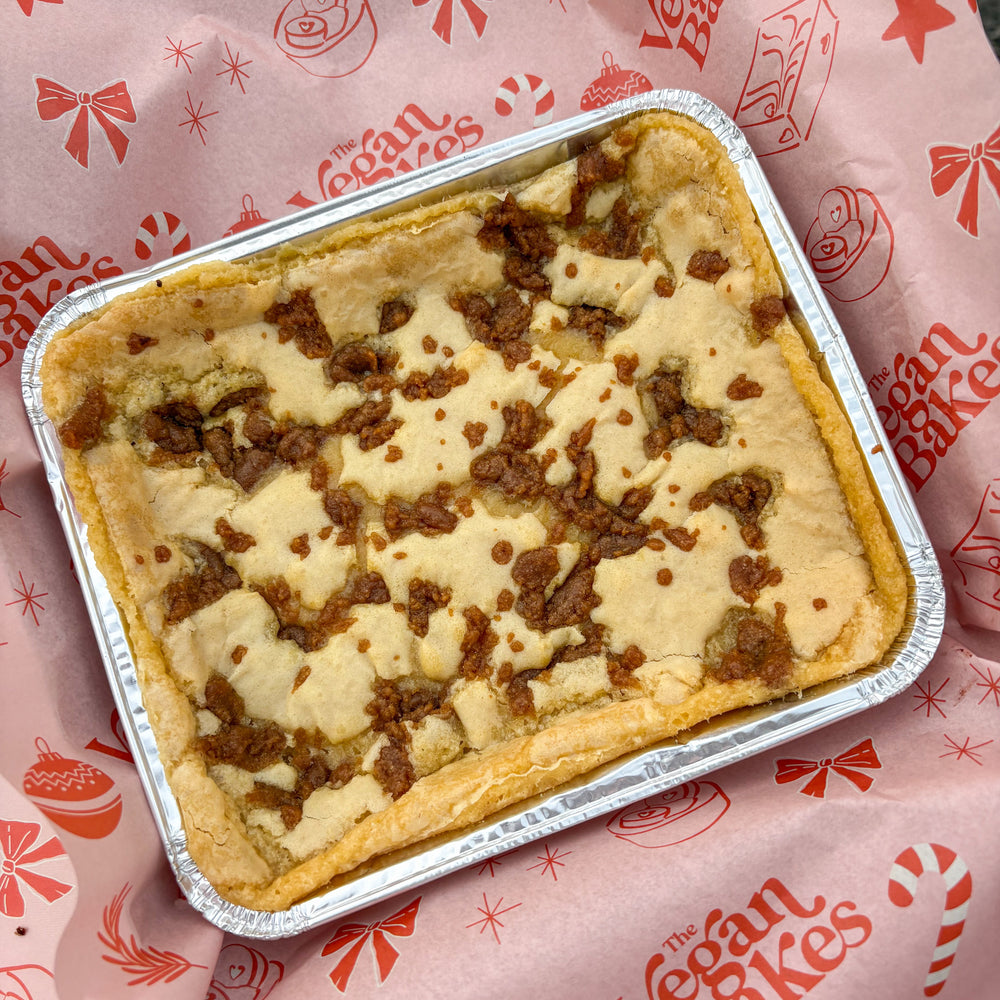 Blondie with gingerbread filling in a metal pan on a pink paper with 'The Vegan Bakes' branding.