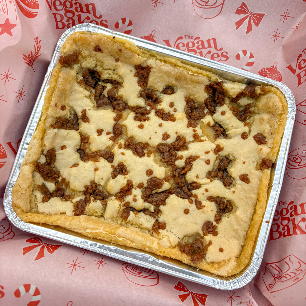 Blondie with gingerbread pieces in a foil tray on branded the vegan bakes paper